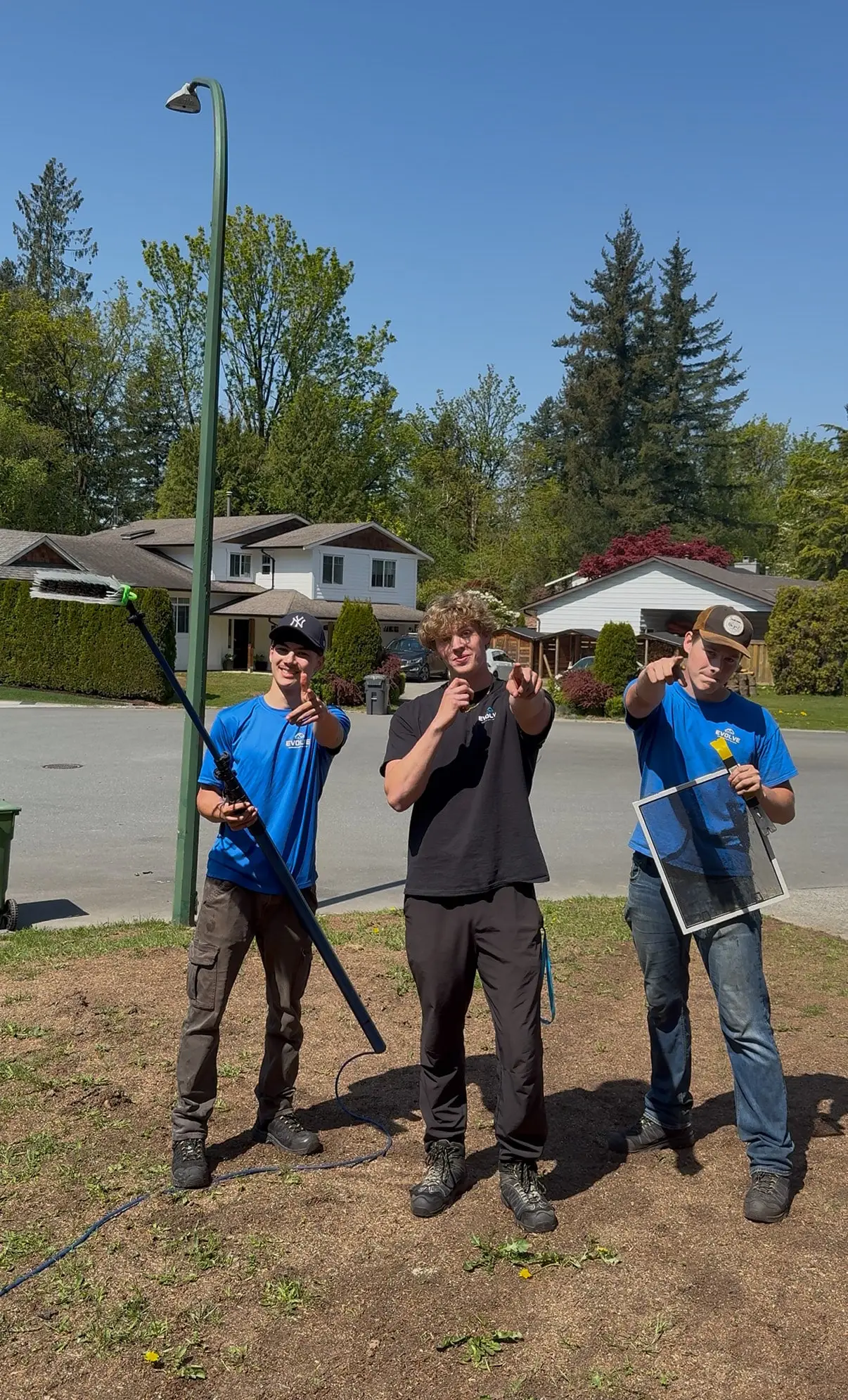 Three Evolve crew members holding water-fed poles and cleaning gear on a front lawn