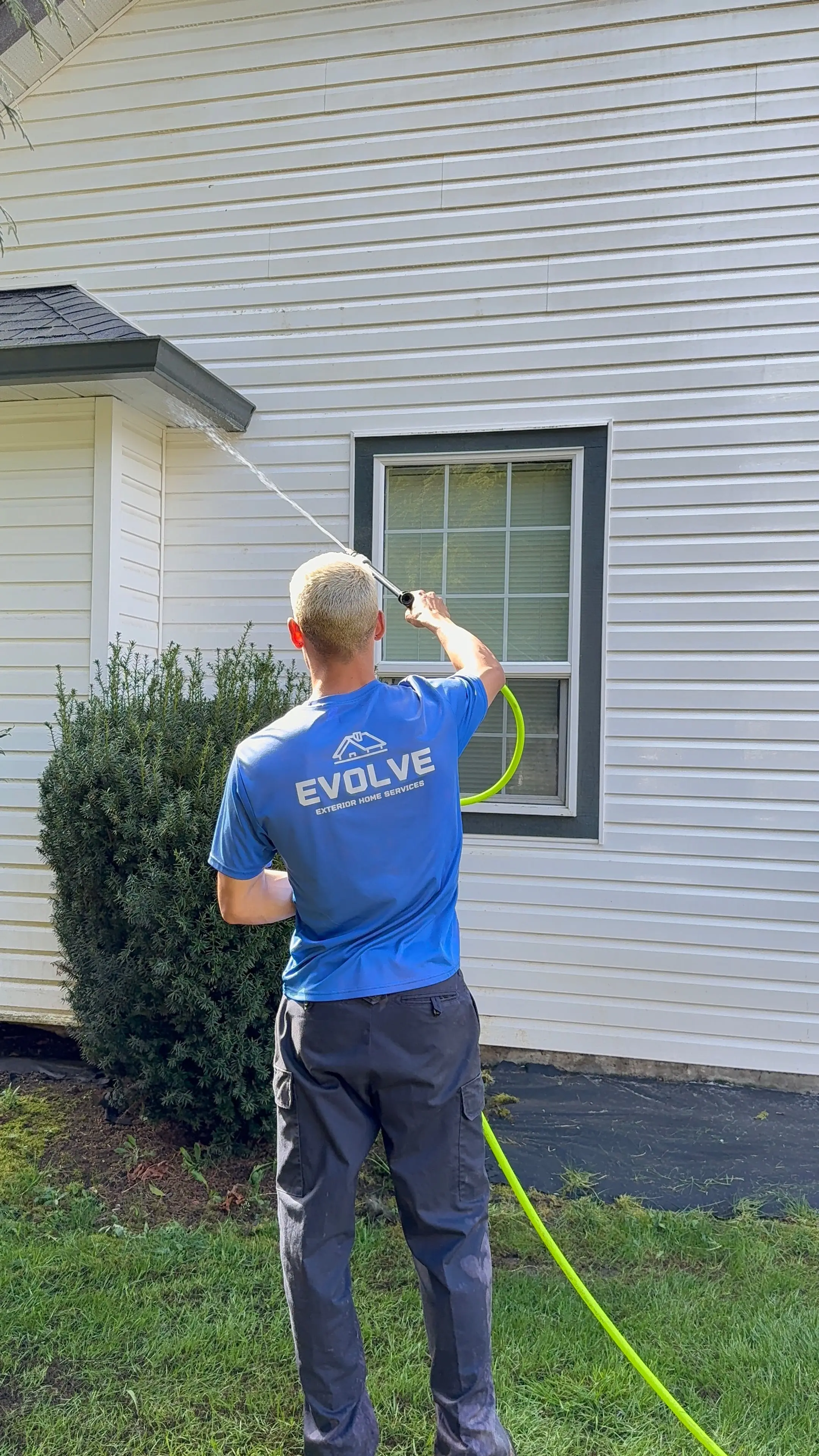 Evolve crew member softwashing the siding of a home with a low-pressure wand