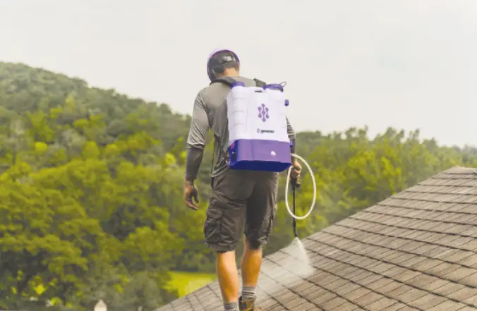 Technician with a backpack sprayer applying GoNano treatment to an asphalt shingle roof