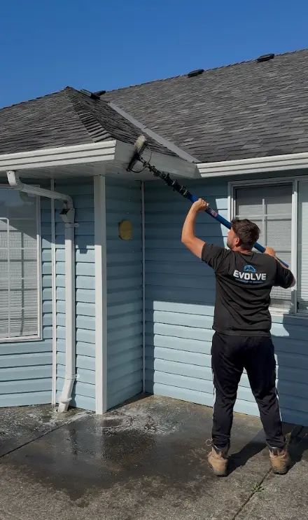 Evolve crew member scrubbing the outside face of a gutter with an extension brush