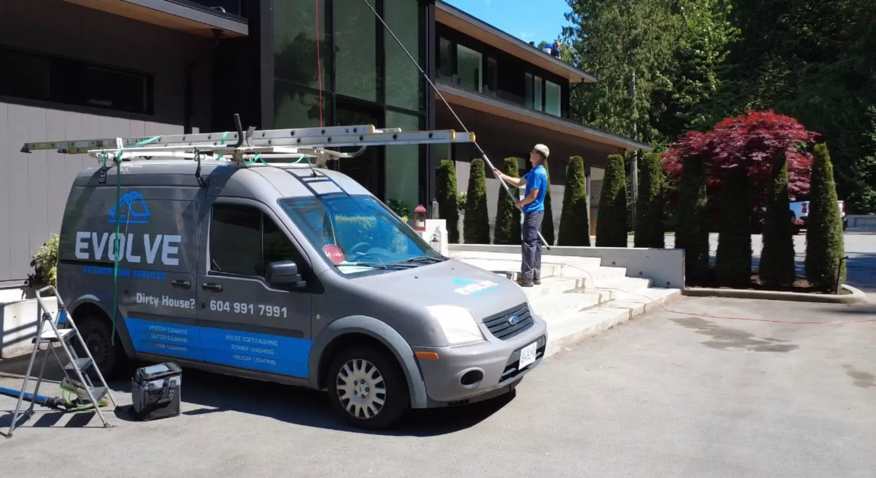Evolve Exterior Home Services van parked in a driveway while a crew member cleans the windows of a large home