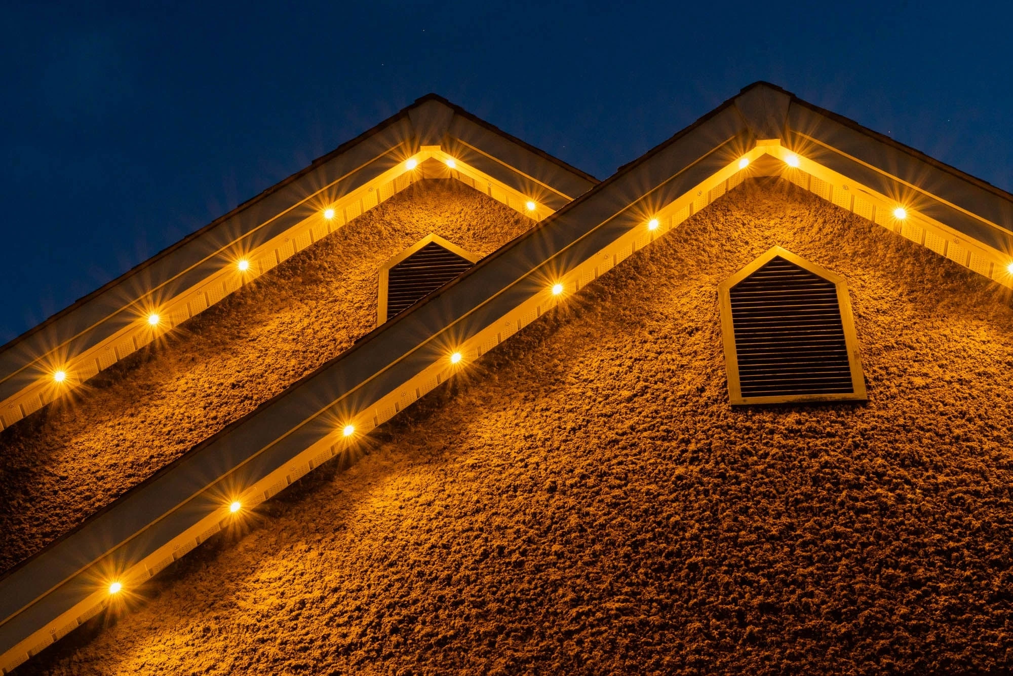 Warm white permanent track lights following two stucco gable peaks at dusk