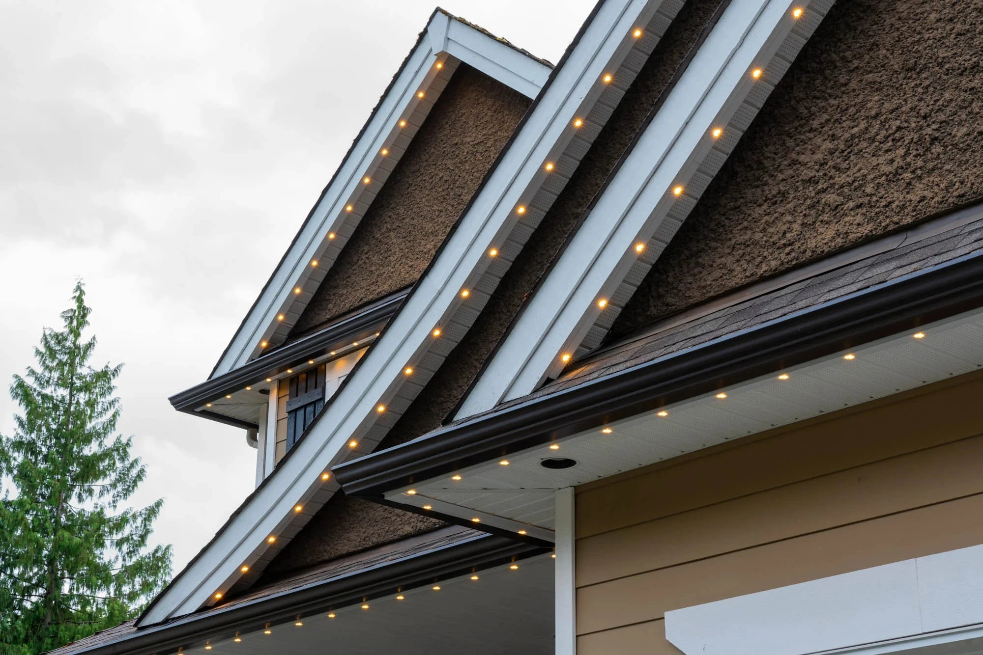 Permanent LED track mitred along layered gable rooflines and a soffit, lit warm white on an overcast day