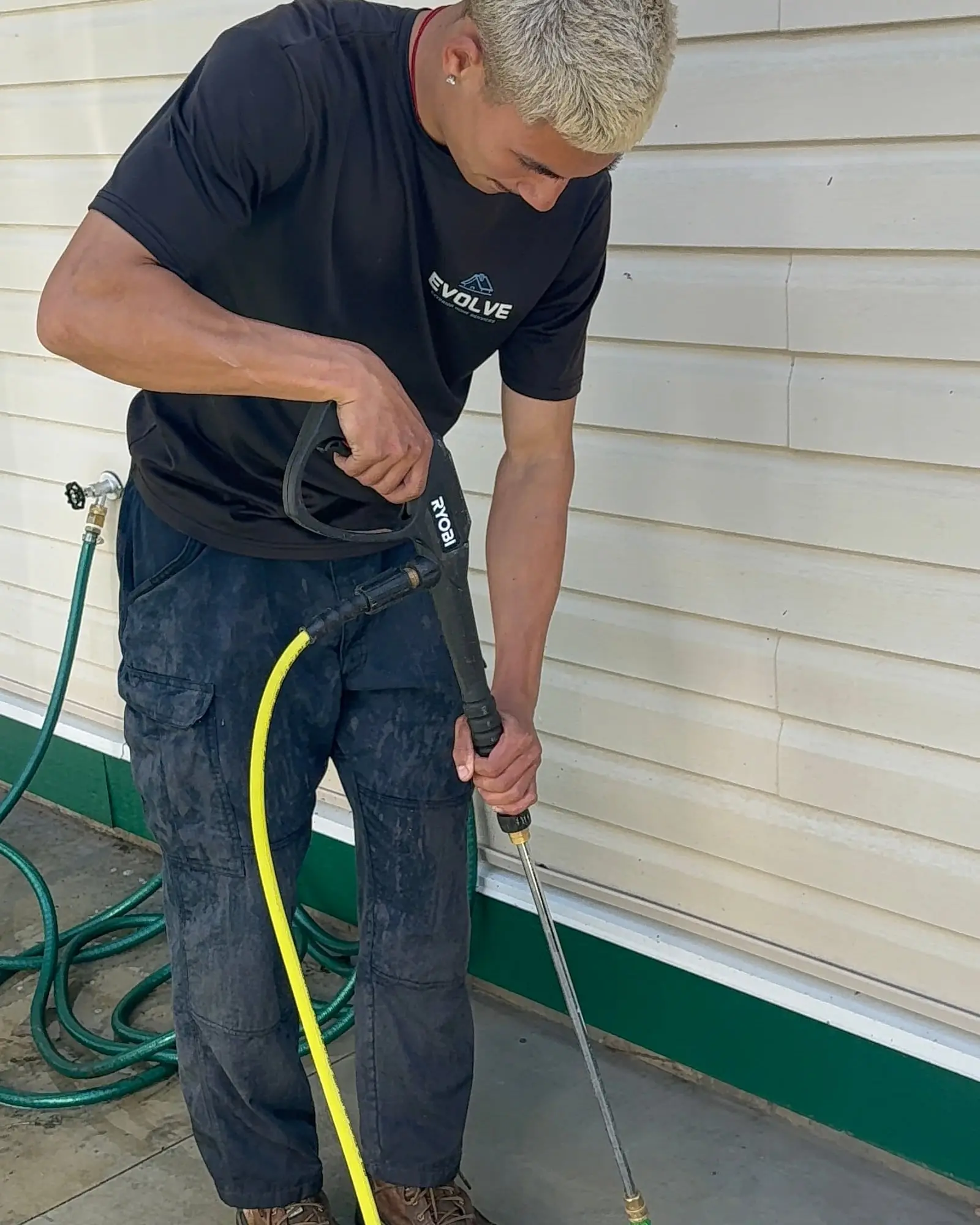 Evolve crew member holding a pressure washing gun and wand beside a home’s siding