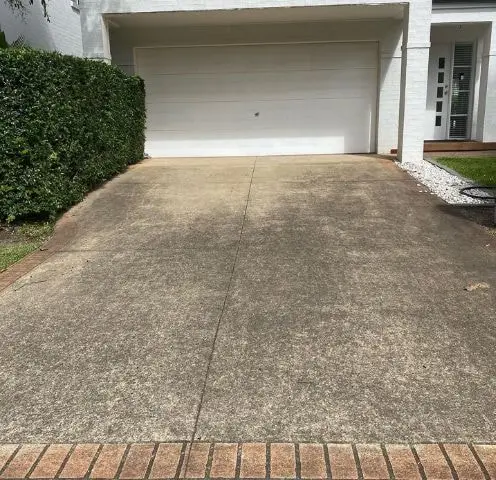 Concrete driveway dark with grime in front of a white double garage and hedge