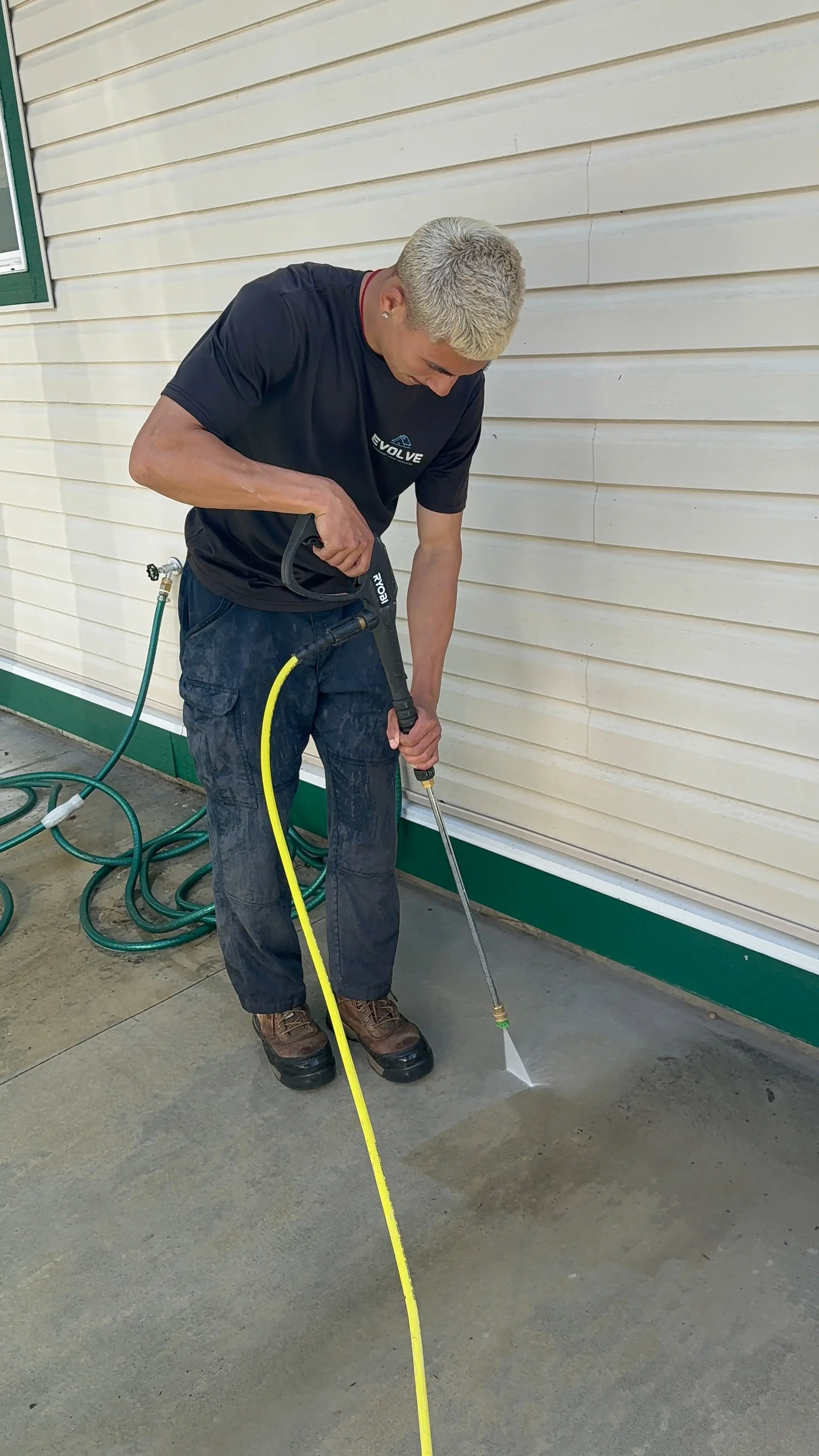 Evolve crew member pressure washing a concrete pad beside a home with a spray wand