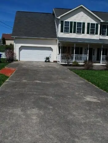 Long concrete driveway dark and stained in front of a white two-storey home