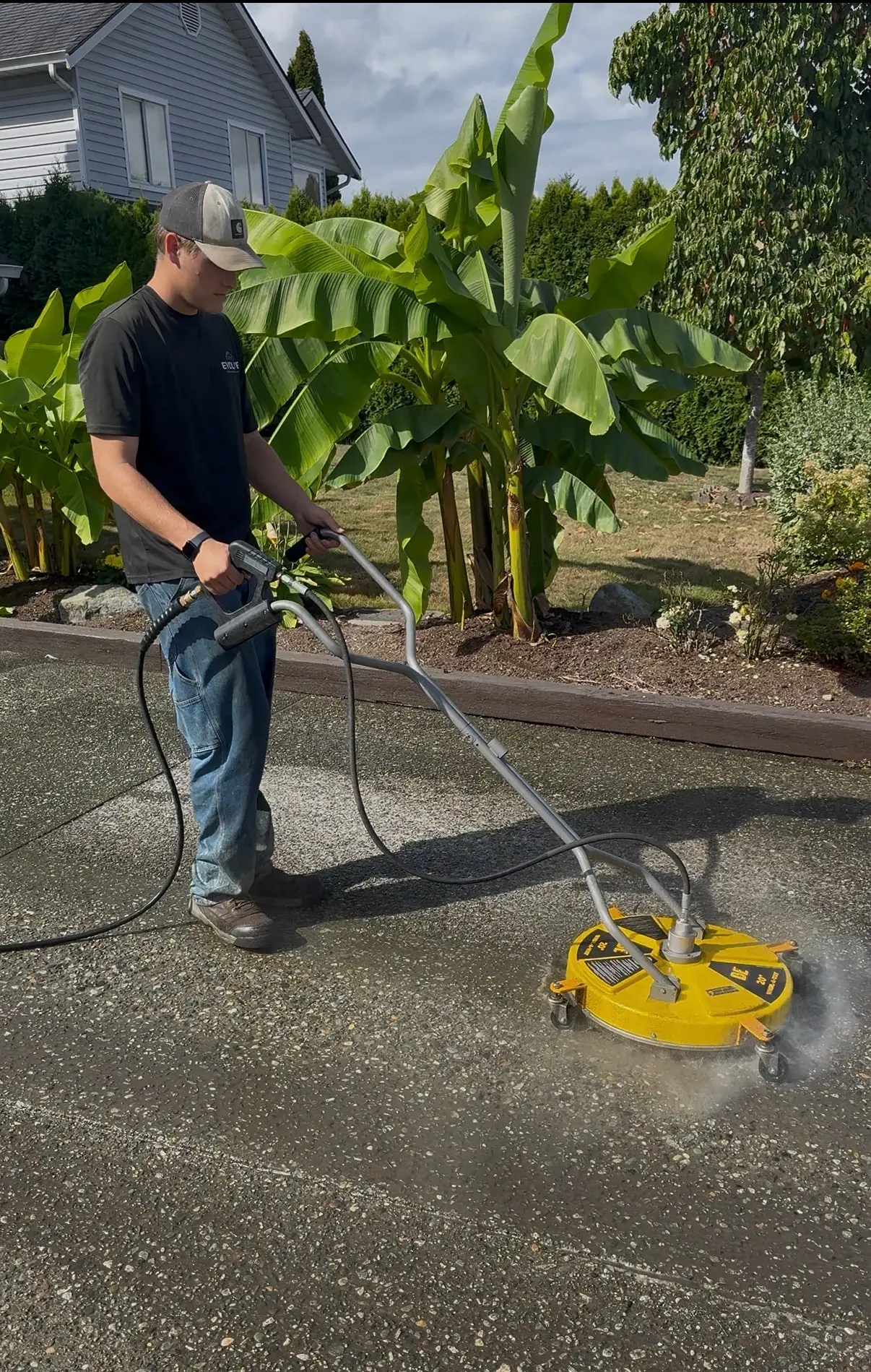 Evolve crew member cleaning a driveway with a yellow rotary surface cleaner