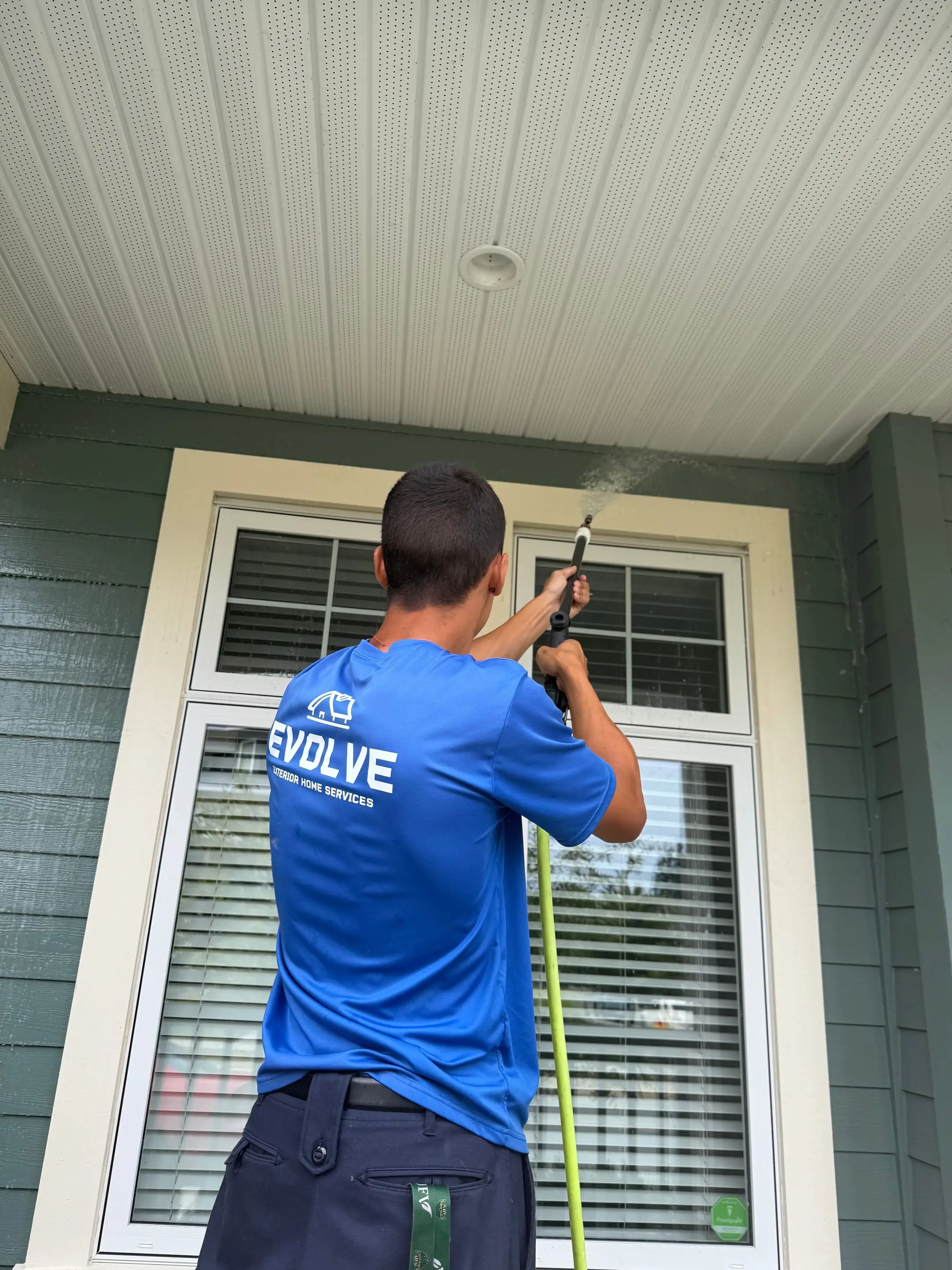 Evolve crew member softwashing green siding and window trim on the front of a home