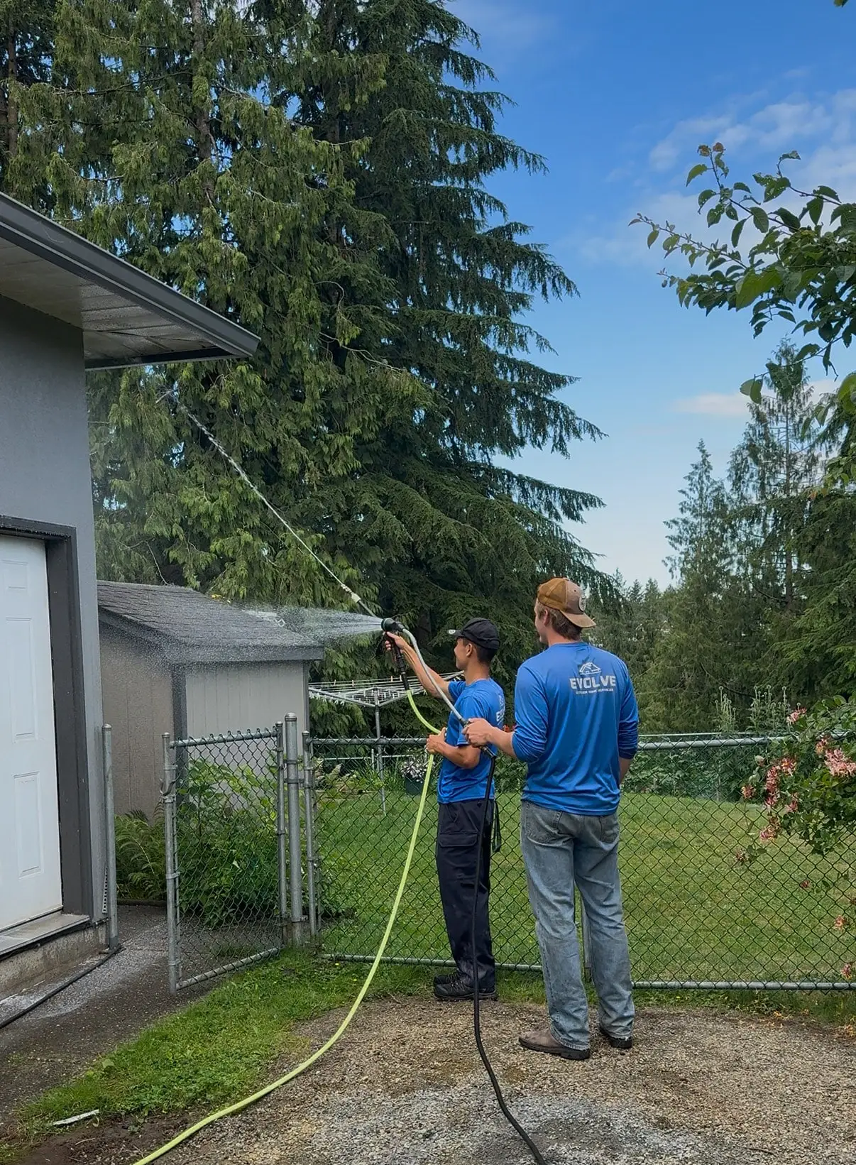 Two Evolve crew members spraying up toward the second storey from the yard