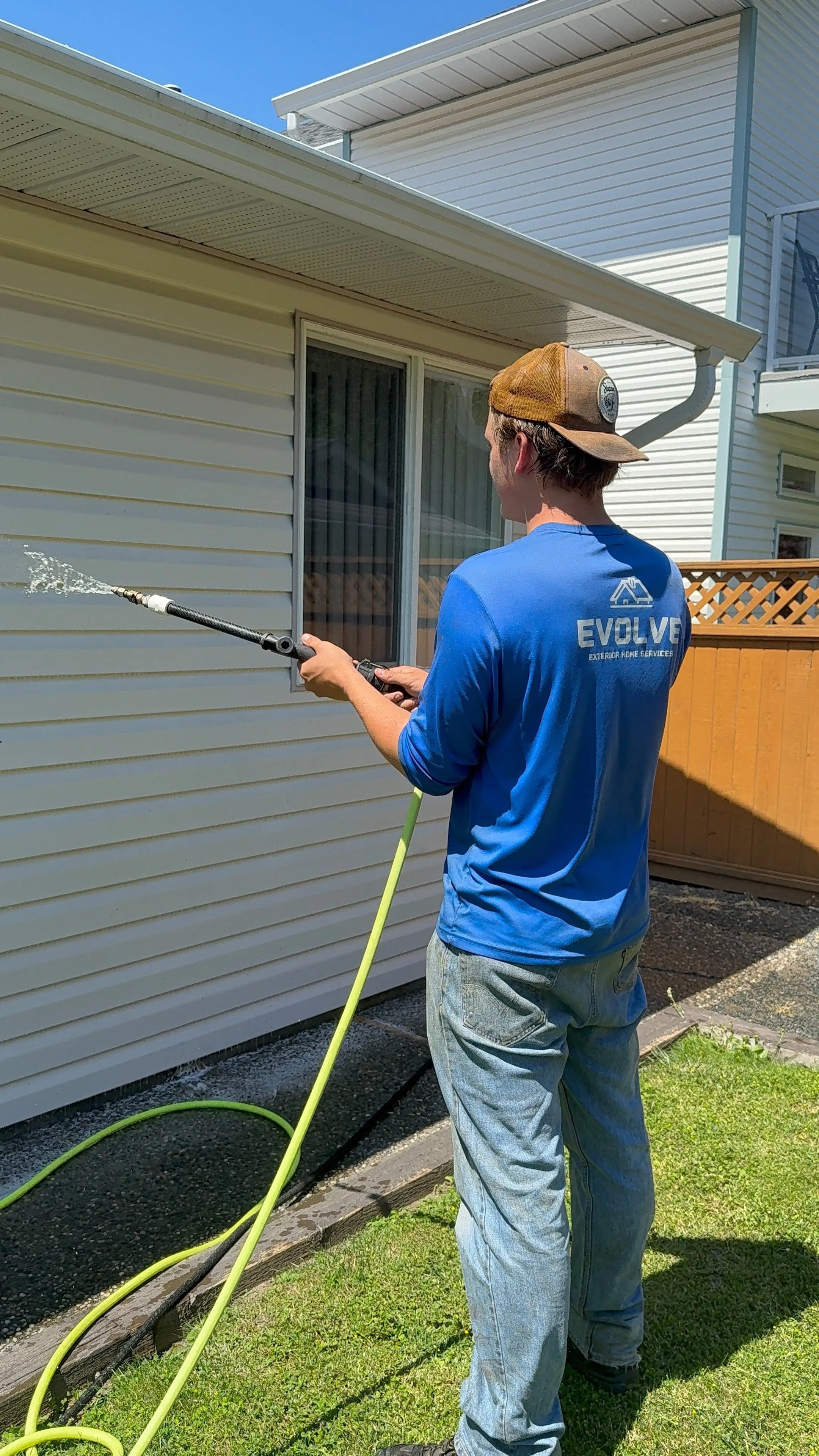 Evolve crew member softwashing white vinyl siding next to a window