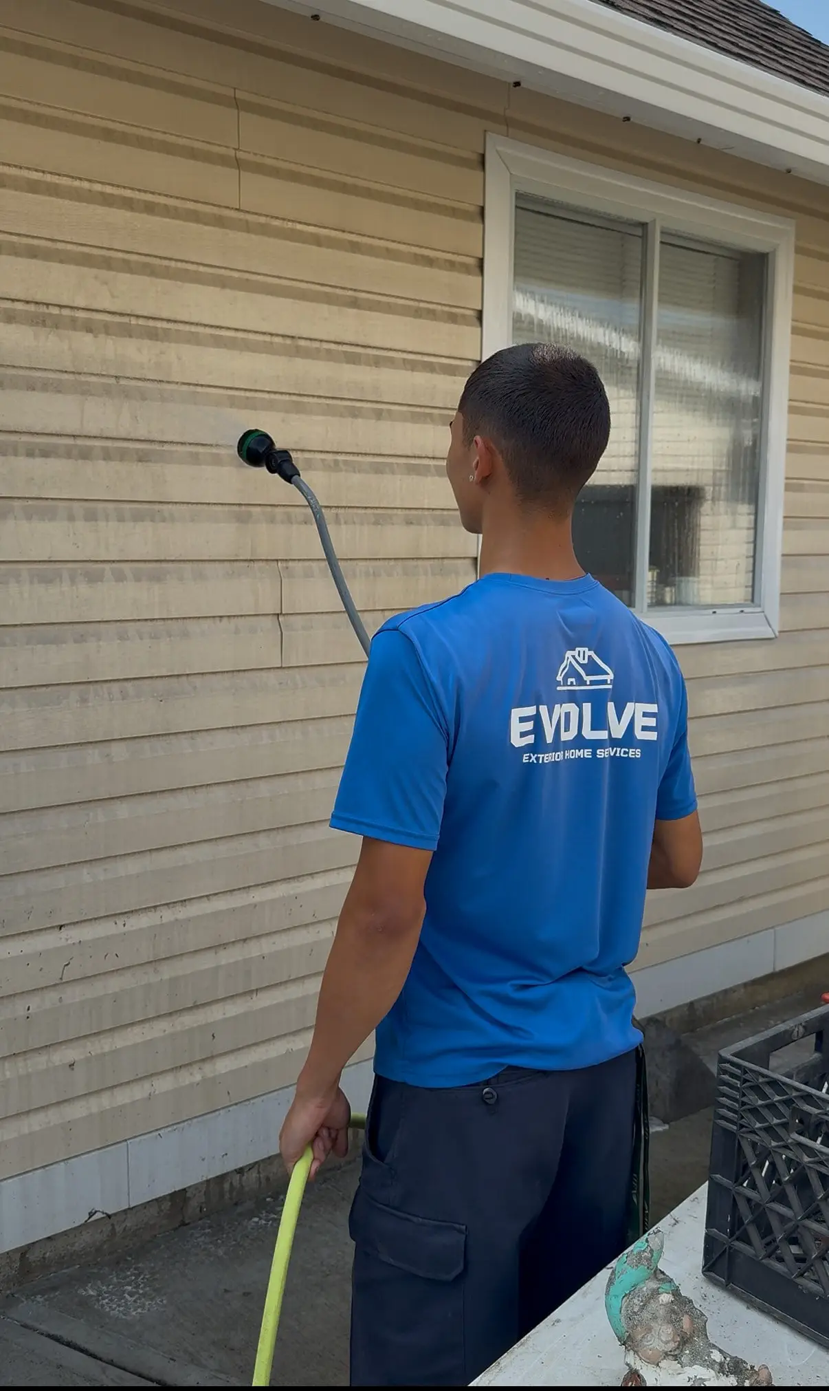Evolve crew member rinsing streaked beige siding with a low-pressure wand