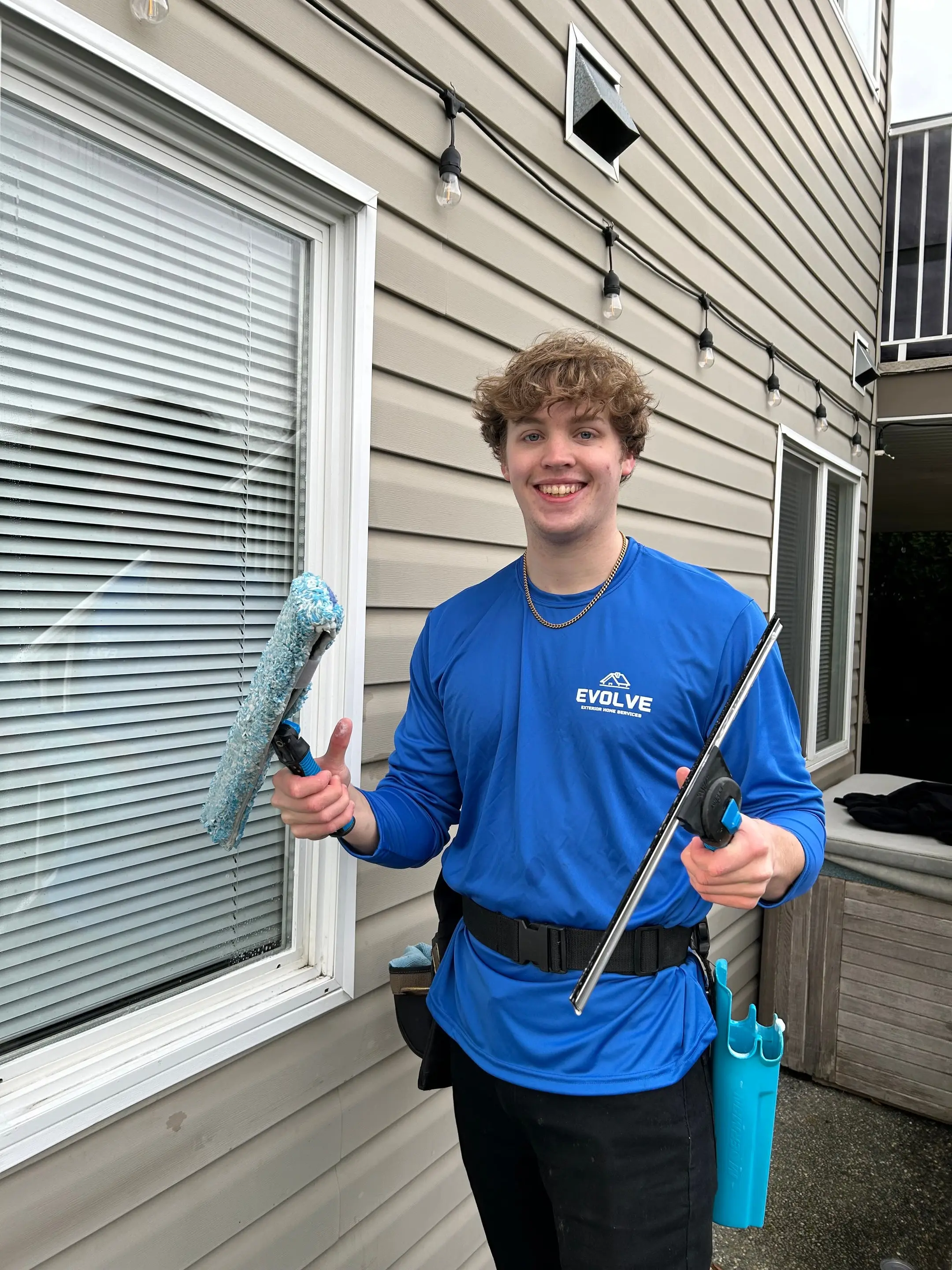 Smiling Evolve crew member holding a squeegee and window scrubber beside a home’s window