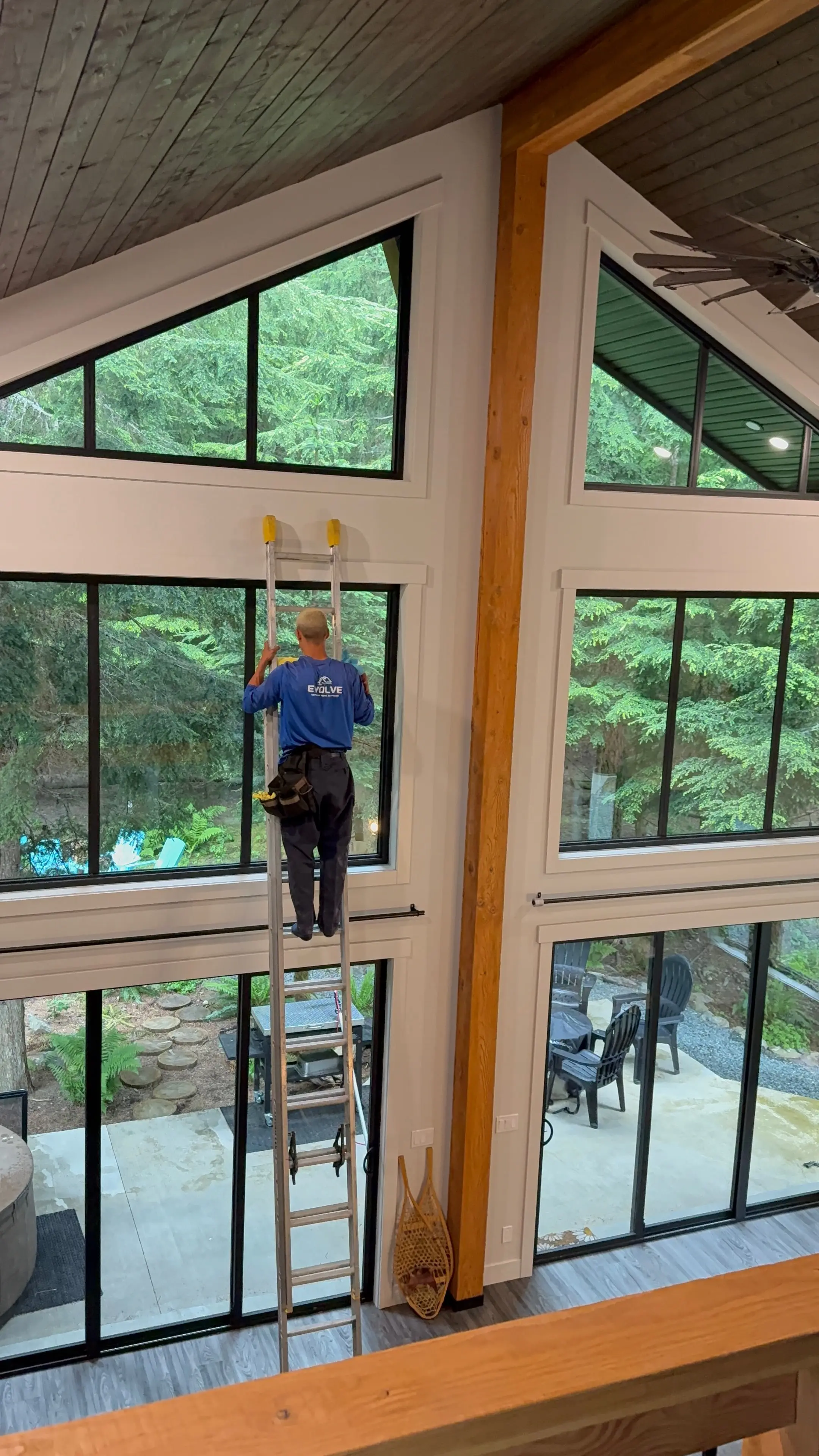 Crew member on a ladder cleaning tall interior windows in a vaulted room