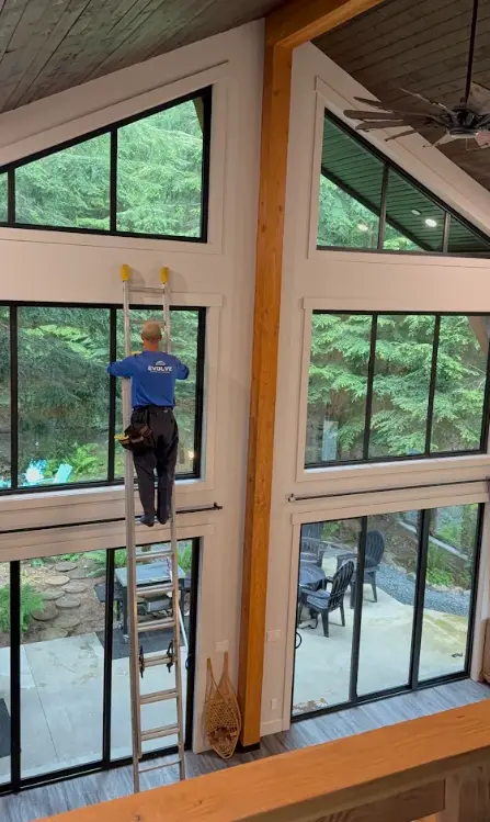 Crew member on a ladder cleaning tall interior windows in a vaulted living room