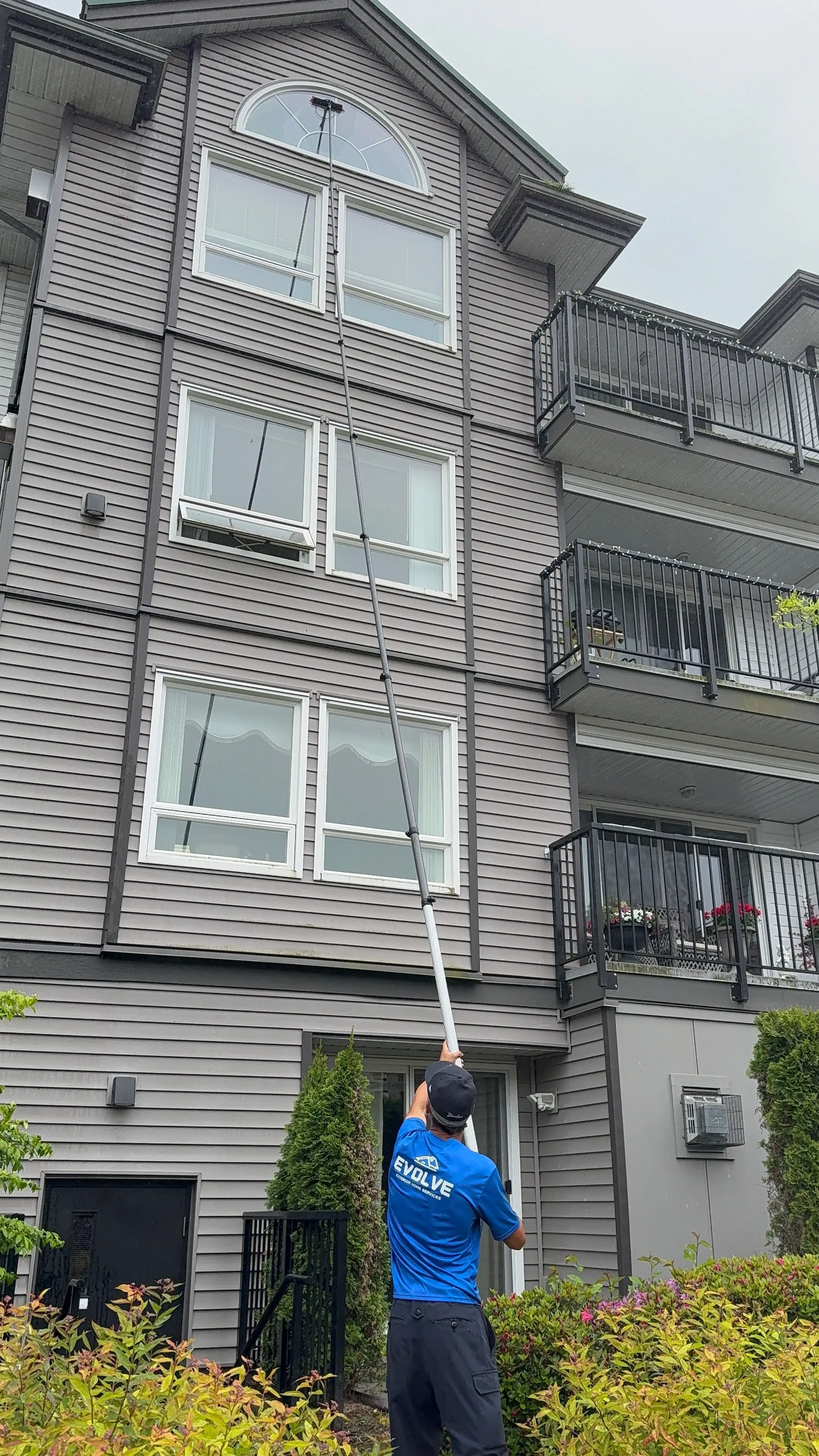 Evolve crew member on the lawn using an extended water-fed pole to reach the upper windows of a tall building