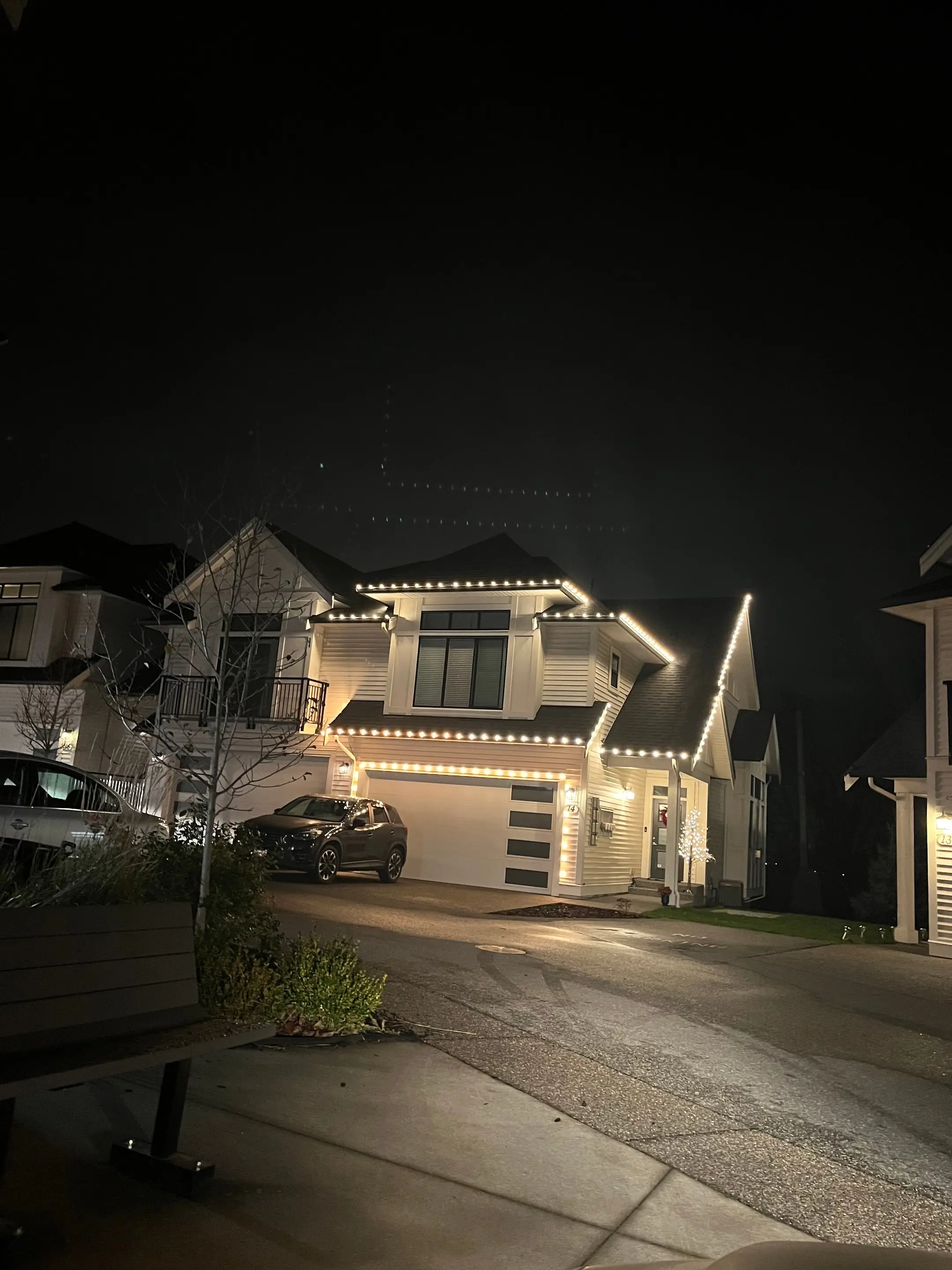 White two-storey home at night outlined in white Christmas lights