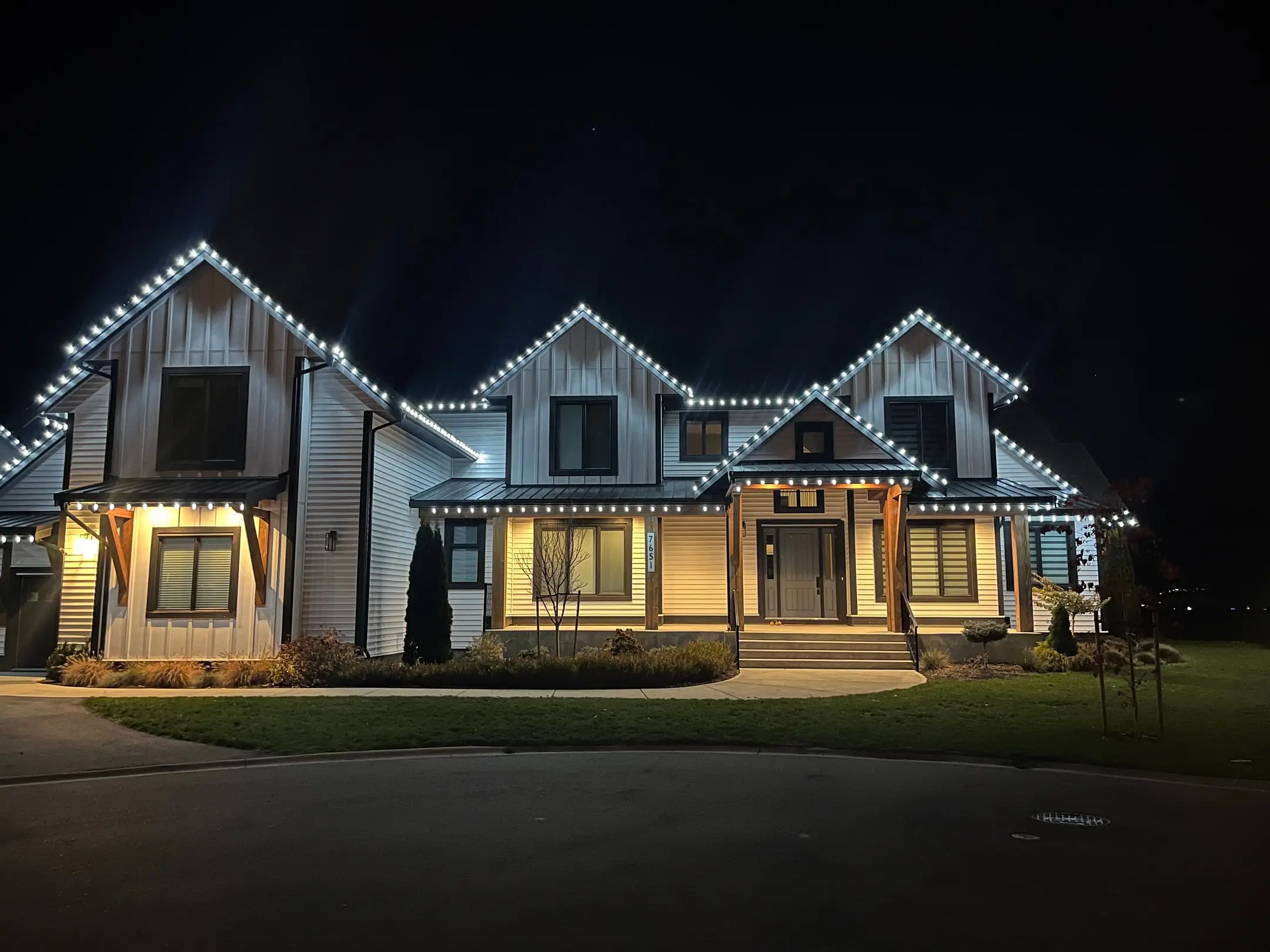 Large two-storey farmhouse at night outlined in white Christmas lights along every gable and roofline