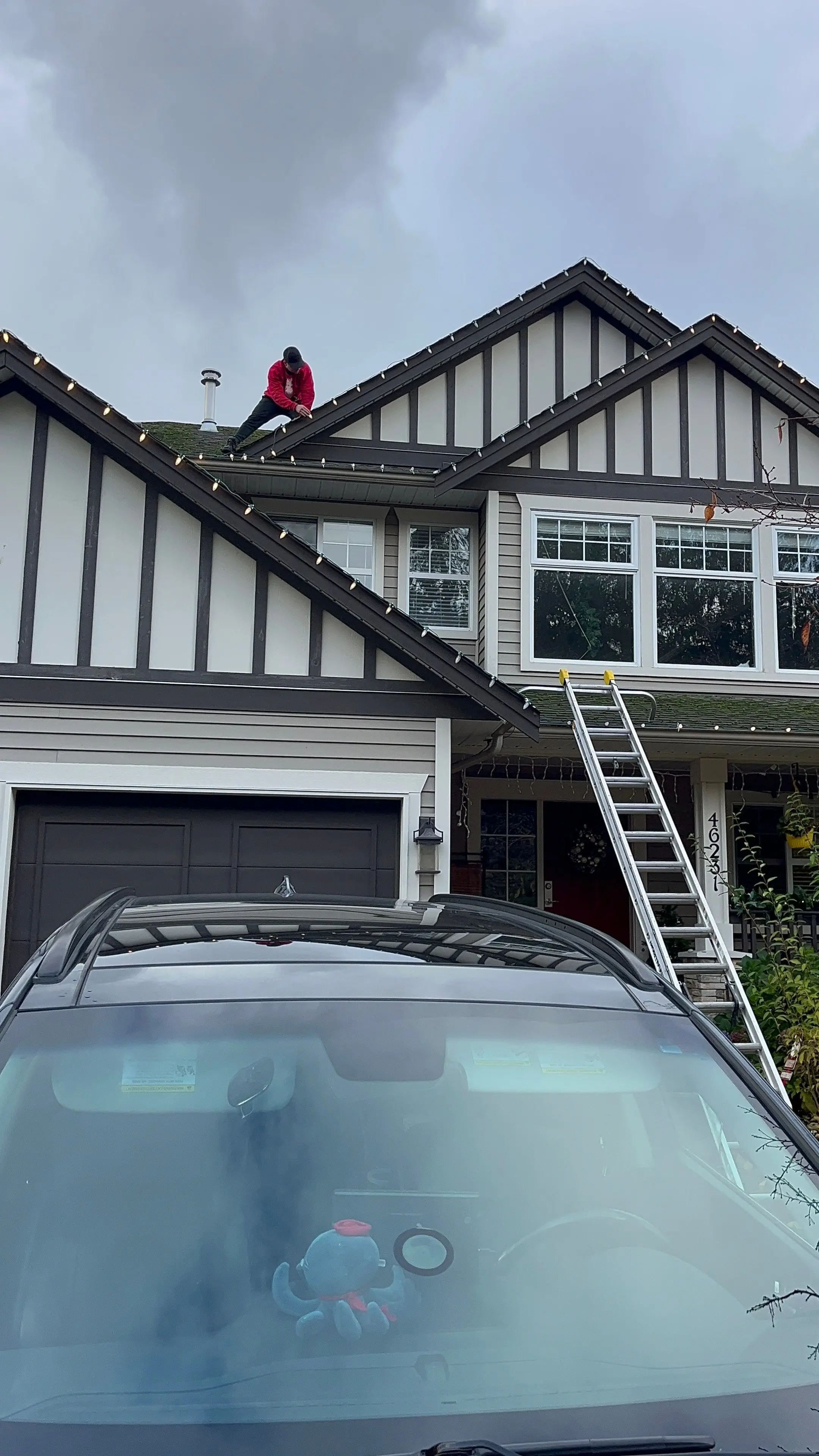 Evolve crew member on a roof installing Christmas lights, with a ladder against the house