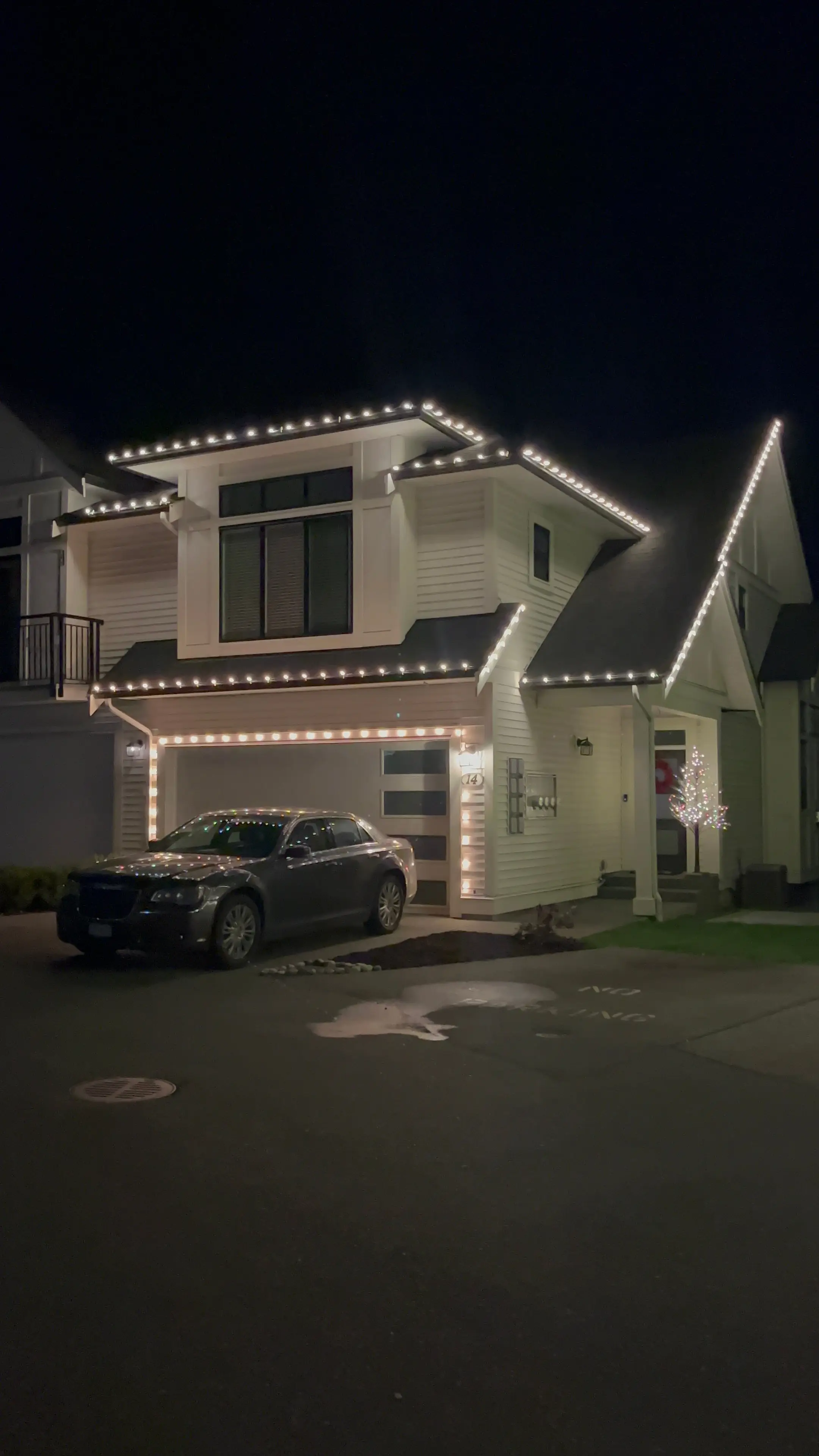 Modern white two-storey home at night with every peak and roofline outlined in white Christmas lights