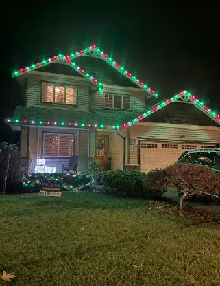 Evolve Holiday Lighting lawn sign in front of a home lit with red and green Christmas lights