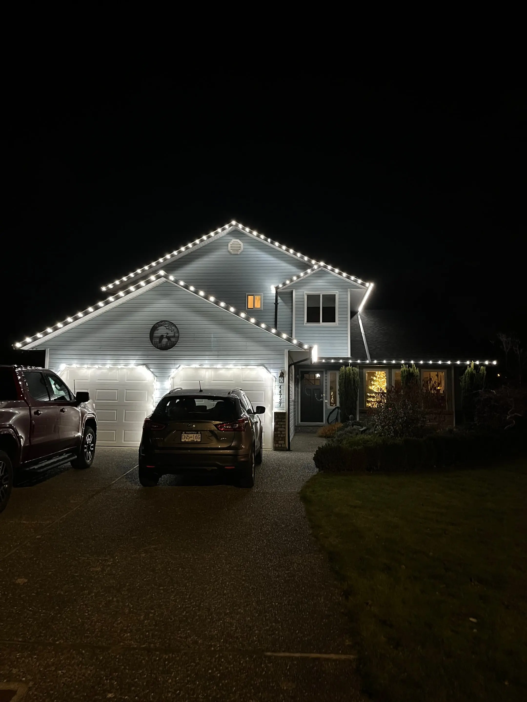 Two-storey home at night outlined in bright white Christmas lights above the garage